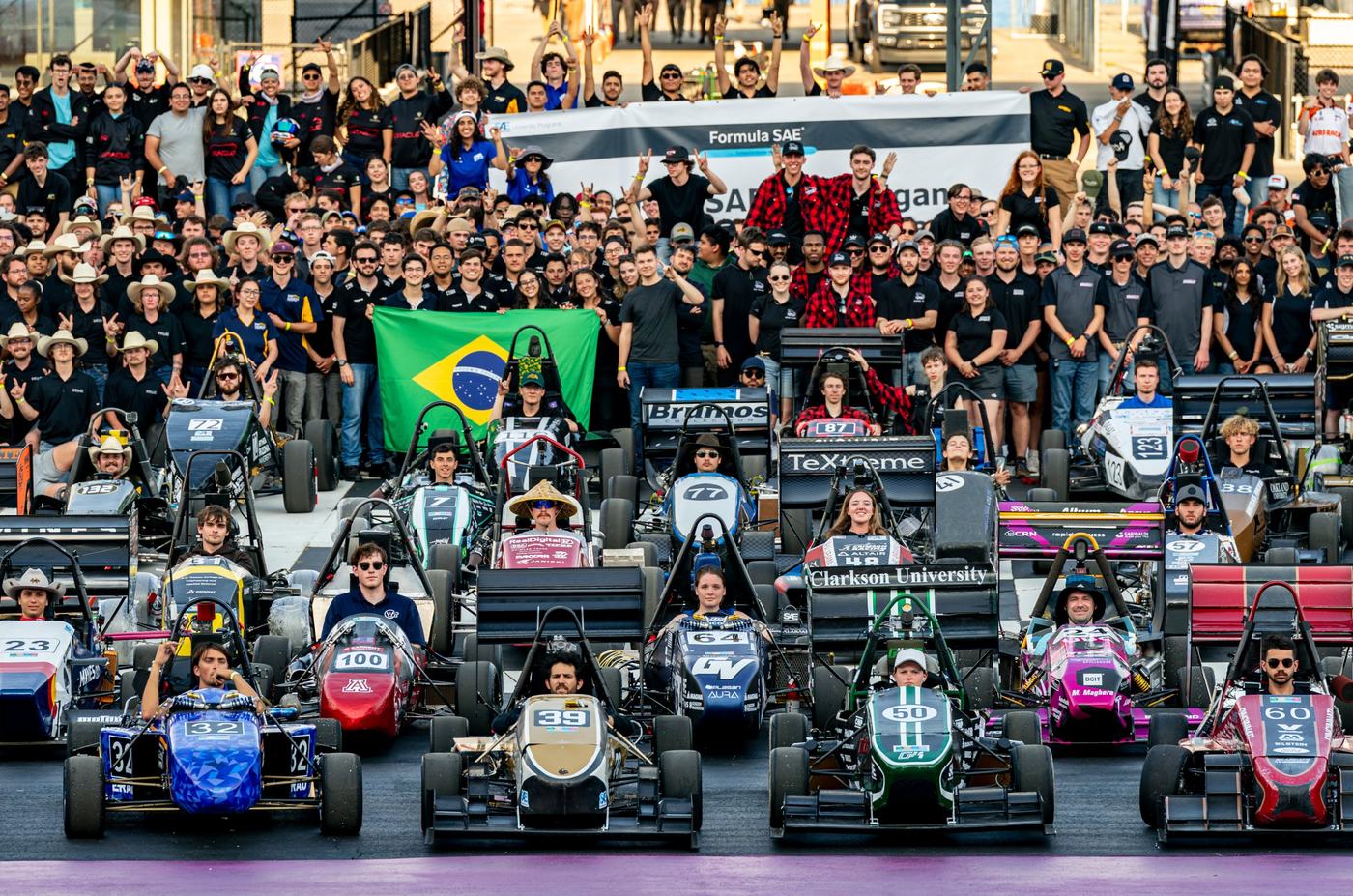 Dozens of Formula SAE cars lined up in front of hundreds of student team members at Formula SAE Michigan