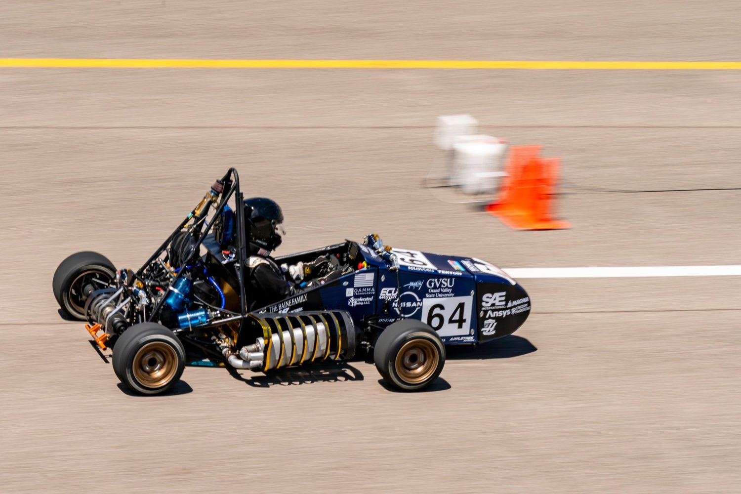Grand Valley State University's navy blue Formula SAE car number 64 at speed past a cone on the track