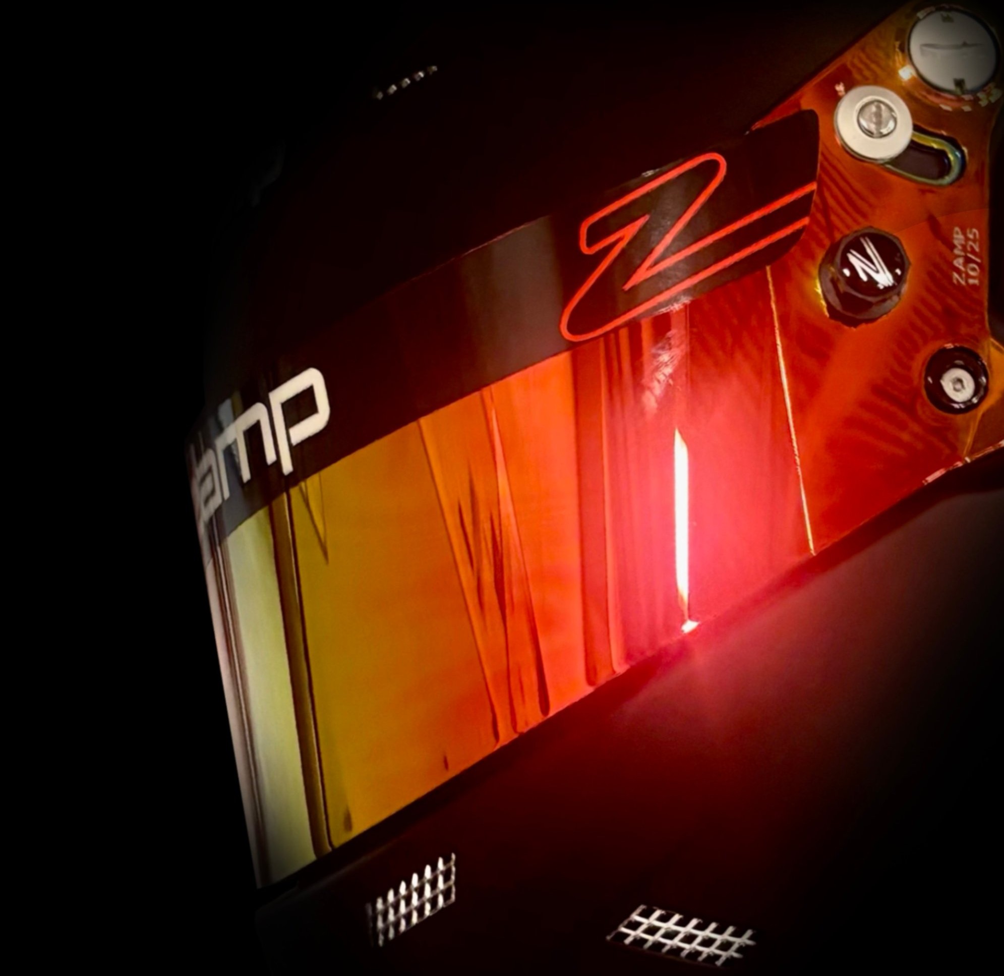 A driver's helmet with a mirrored red and gold visor, lit in a dark shop