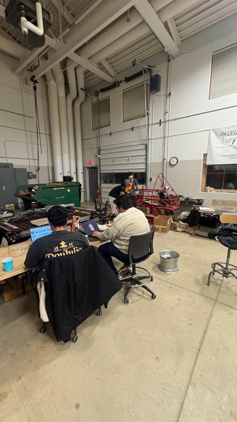 Members at laptops in the shop with the red frame behind them