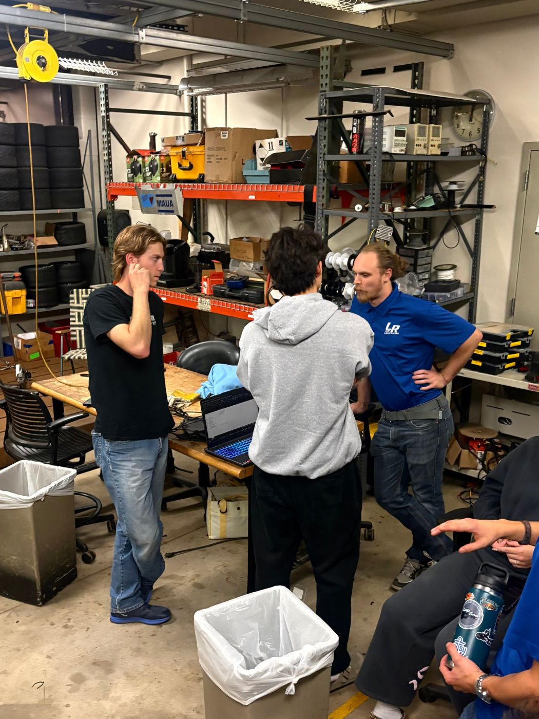 Calvin and Laker Racing members talking at a workbench with a laptop